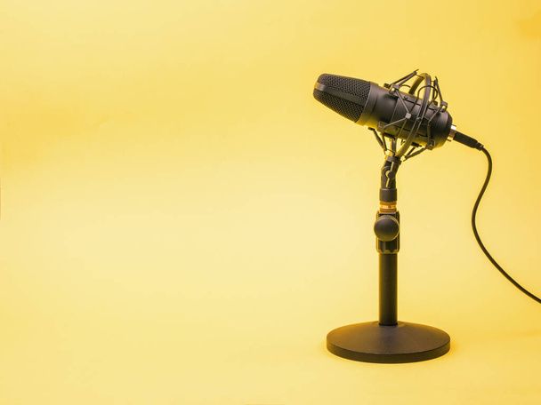 Een gele achtergrond en een moderne condensator microfoon. Geluidsopnameapparatuur. - Foto, afbeelding