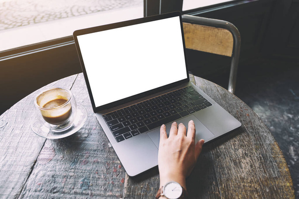Mockup-Bild einer Frau, die ein Laptop-Touchpad mit leerem weißen Desktop-Bildschirm auf einem Holztisch benutzt und berührt - Foto, Bild