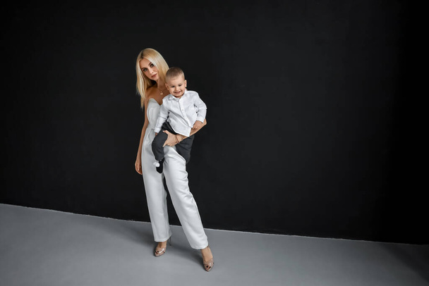 Fashionable mom in a white elegant outfit and a baby on a black background. Feminism concept, mother's day - Fotografie, Obrázek