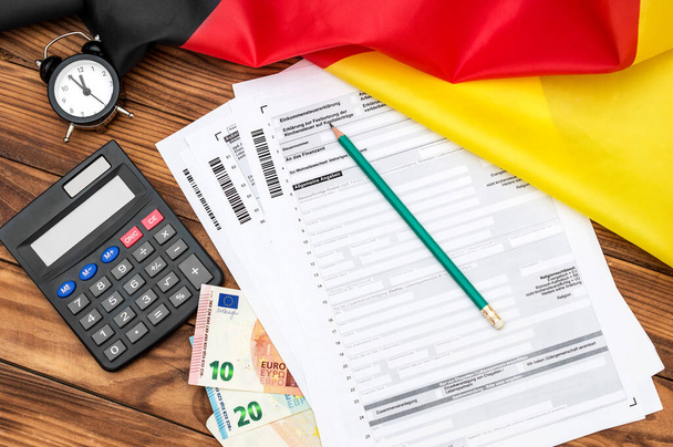 計算機とテーブルの上にフラグを持つドイツの税務フォーム。翻訳: (所得税申告書、資本所得、適用従業員の貯蓄、損失運送状、税番号、税務署、住居の変更、一般情報、課税対象者) - 写真・画像