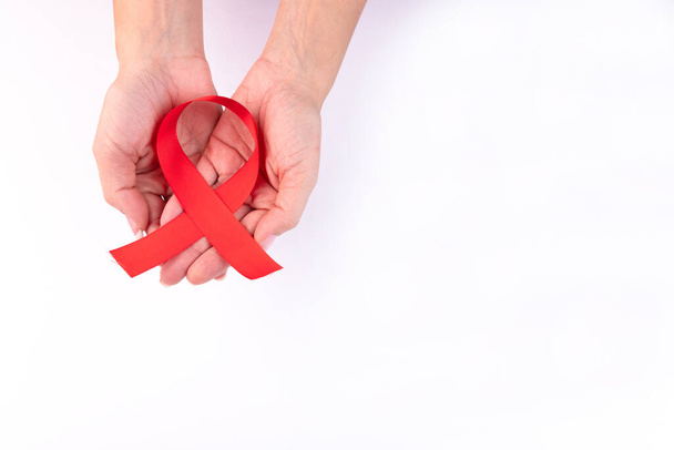 Rood lint in vrouwelijke handen als symbool van aids bewustzijn op een witte achtergrond. - Foto, afbeelding