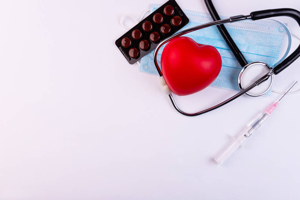 Volumetric heart with a phonendoscope, syringe and pills on a white background. The concept of support for patients with heart disease. - Fotó, kép