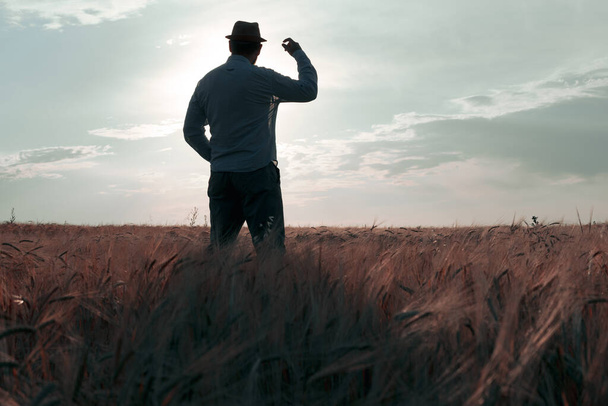 un homme avec un chapeau se tient sur le terrain à l'aube avec son dos à nous. un regard vers l'avenir pour rencontrer un nouveau jour - Photo, image
