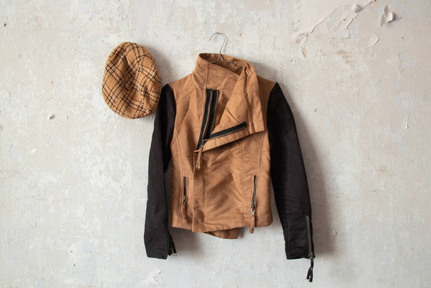 a brown women's jacket and a plaid cap hang on a white wall at home - Photo, Image