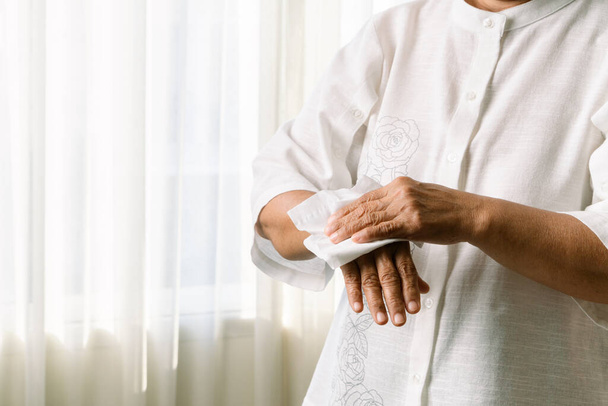 Az idősebb nő fehér lágypapírral tisztítja a kezét. fehér alapon elkülönítve - Fotó, kép