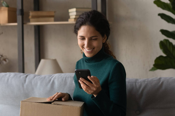 Smiling woman unpack box shopping on smartphone - 写真・画像