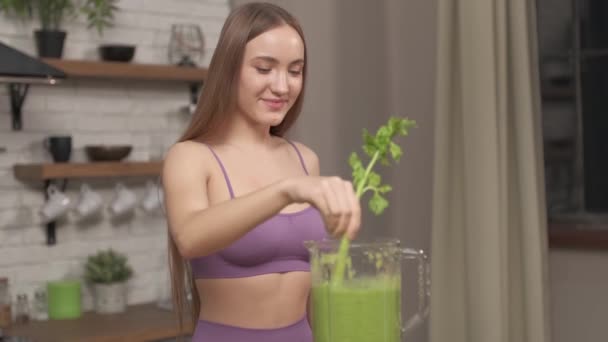 Sportif Kadın blenderlı yeşil sebze suyu yapıyor, dolduruyor, içiyor. Sağlıklı beslenme tarzı, mutfakta evde kereviz ve ıspanakla meyve kokteyli hazırlayan genç bir kadın. Kerevizli blender ile smoothie karıştıran kız - Video, Çekim
