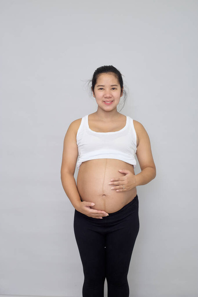Sonriendo embarazada mujer asiática tocando su vientre sobre fondo gris - Foto, imagen