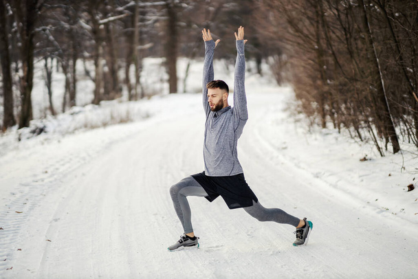 Fit sportsman doing warm up exercises in nature on snow at winter. Healthy habits, winter sport - Photo, Image