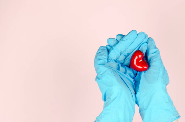 Hands in blue medical gloves hold a heart on a pink background. Health care concept - Фото, зображення