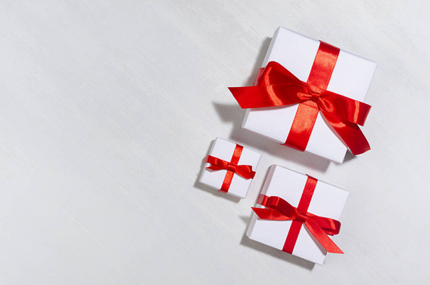 Festive background for sale with white gift boxes with red silk ribbon in sunlight with shadow on white wood board, top view, border. - 写真・画像