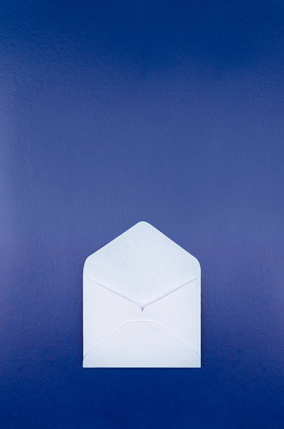 Open blank white envelope on dark blue background, top view, copy space, mockup, vertical.  - Photo, Image