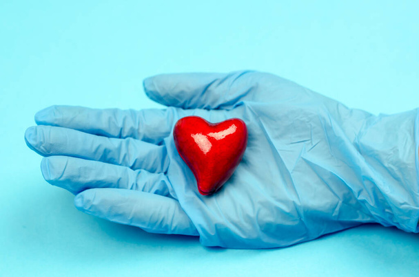 Mavi eldivenli eller mavi arka planda bir kalp tutuyor. Sağlık hizmeti konsepti. Dünya Kalp Günü - Fotoğraf, Görsel