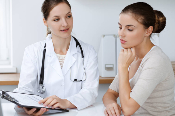 Doctor and patient are sitting and discussing health examination results in clinic office. Health care, medicine and good news concepts - Foto, imagen