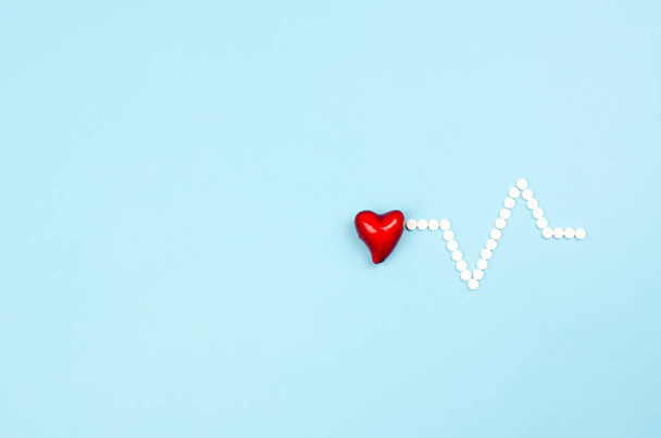 Corazón rojo y pastillas en forma de cardiograma sobre fondo azul - Foto, imagen