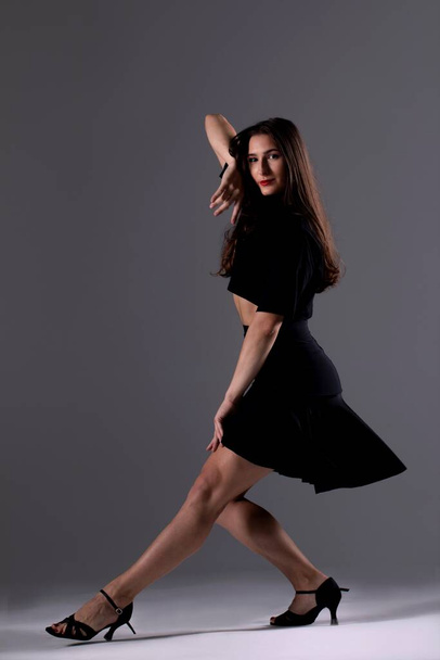 Молодая профессиональная танцовщица, практикующая в студии, девушка в черном платье, танцовщица - Фото, изображение