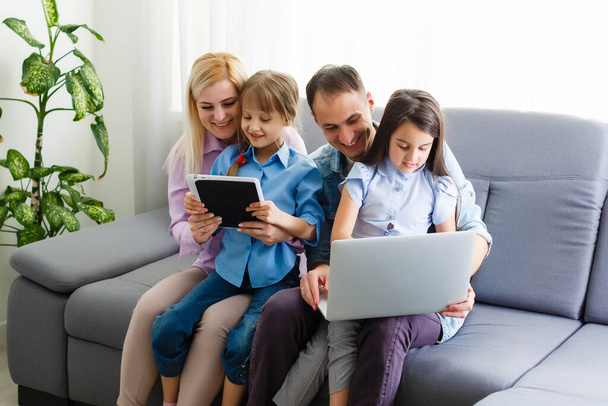 Happy family of four parents and cute little kids children enjoy using the tablet, watching cartoons, make internet video call or shopping online looking at computer screen sit together at home - Photo, Image