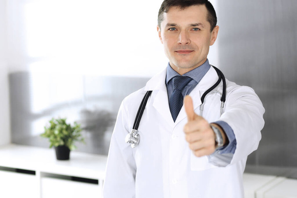 Доктор человек веселый улыбается в камеру, большие пальцы вверх. Идеальное медицинское обслуживание в клинике. Счастливого будущего в медицине и здравоохранении - Фото, изображение