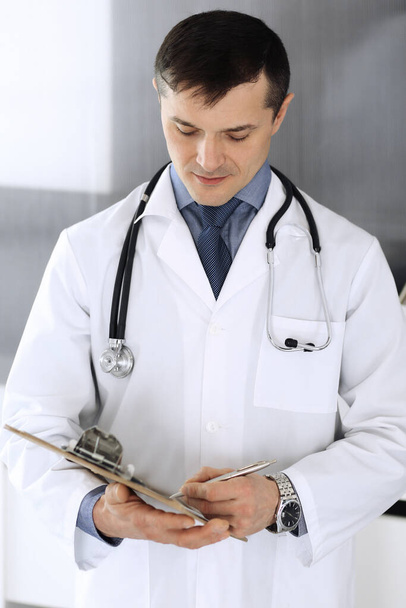 Doctor man using clipboard for filling up medication history records. Perfect medical service in clinic. Physician at work in hospital. Medicine and healthcare concepts - Foto, Bild