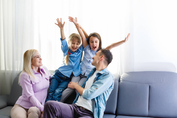 Fröhliche junge Familie mit lachenden Kindern, die zusammen auf der Couch sitzen, Eltern mit Kindern, die sich zu Hause amüsieren - Foto, Bild