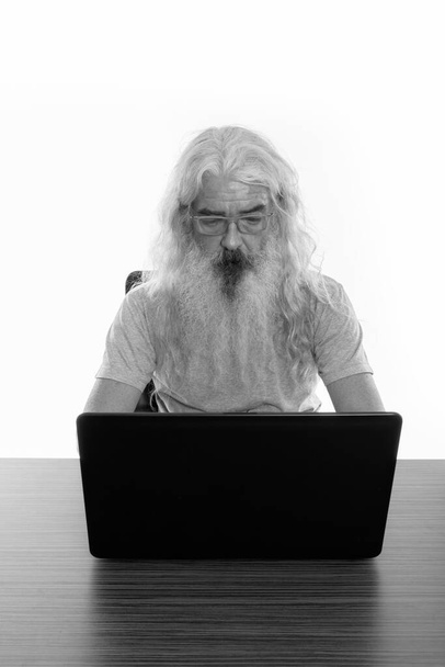 Homme barbu senior portant des lunettes tout en utilisant un ordinateur portable sur une table en bois - Photo, image