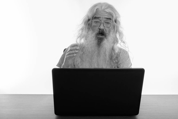 Yaşlı sakallı adamın, tahta masada dizüstü bilgisayar kullanırken şok olmuş görüntüsü. - Fotoğraf, Görsel