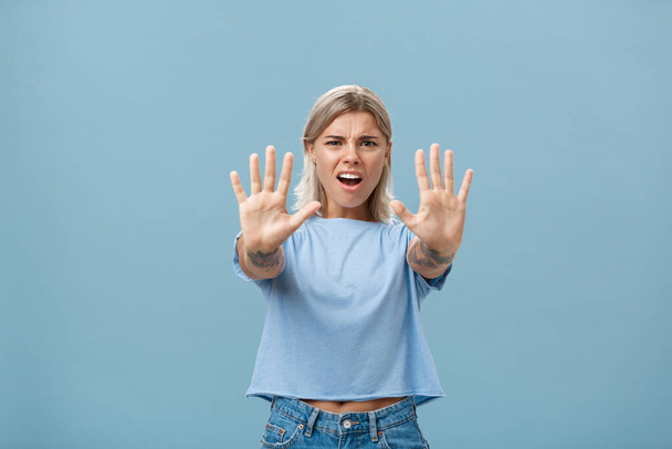 Álljon meg! Portré intenzív elégedetlen és irritált vonzó fiatal nő kék pólóban húzza a kezét a kamera felé megállás vagy nem gesztus ráncolás és bosszús kifejezés - Fotó, kép