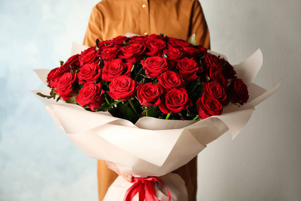 Woman holding luxury bouquet of fresh red roses on light background, closeup - Foto, immagini