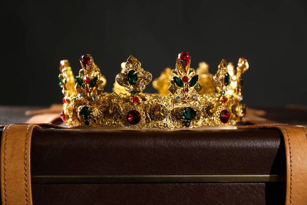 Beautiful golden crown on suitcase against black background. Fantasy item - Foto, afbeelding