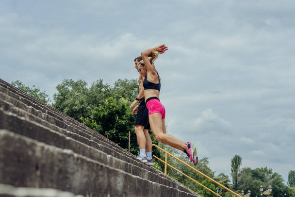 Debajo de la vista de jóvenes atletas masculinos y femeninos saltando arriba en la escalera al aire libre - Foto, imagen