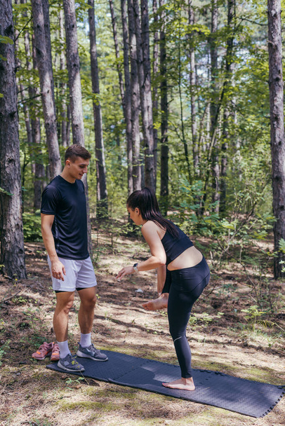 A beautiful young fitness couple is preparing for stretching before running in the forest. - Φωτογραφία, εικόνα