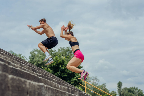 Abaixo vista de jovens atletas masculinos e femininos pulando no andar de cima na escada ao ar livre - Foto, Imagem