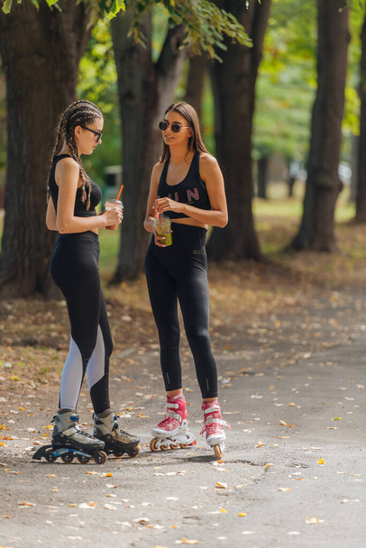 Two women in sportswear rollerblading at the park in sunny weather. - Zdjęcie, obraz