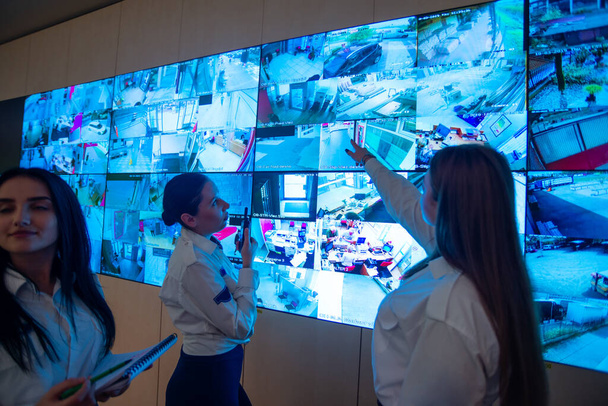 Φύλακες ασφαλείας που στέκονται μπροστά από μια μεγάλη οθόνη CCTV στην κύρια αίθουσα ελέγχου, ενώ διαβάζετε και συζητάτε τα σχέδια - Φωτογραφία, εικόνα