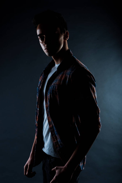 Cool young man dressed in shirt posing in modern studio against black background - Photo, Image