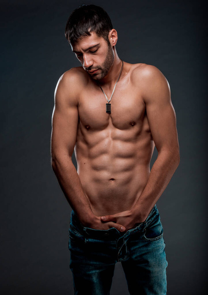Studio body shot of an attractive man posing shirtless in blue denim pants - Photo, Image