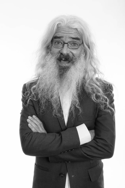 Estudio de tiro de feliz hombre de negocios barbudo mayor sonriendo mientras llevaba gafas con los brazos cruzados - Foto, Imagen