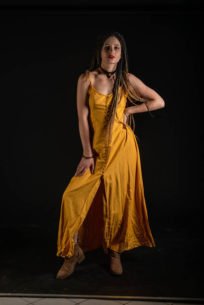 Mystic ancienne déesse reine portant une robe jaune sur un fond isolé studio noir. Femme féministe portant des tresses et posant dans un studio. - Photo, image