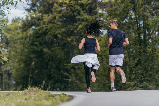 Young fit couple atheltes running on running road in a forest. - Photo, Image