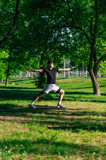 Atractivo joven caucásico estirándose y haciendo ejercicios de yoga sobre la hierba verde en el parque - Foto, Imagen
