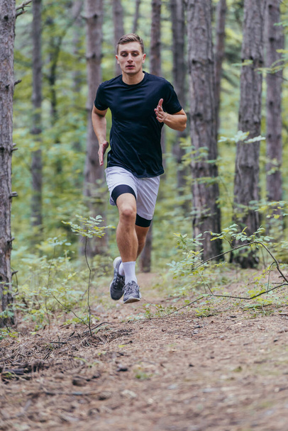 Quadro completo di un attraente atleta di sesso maschile che corre nel bosco - Foto, immagini