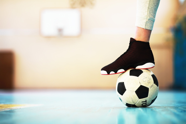 Egy emberi láb pihenés a betonpadlón. Fénykép egy focilabdáról és tornacipőről egy fapadlón - Fotó, kép