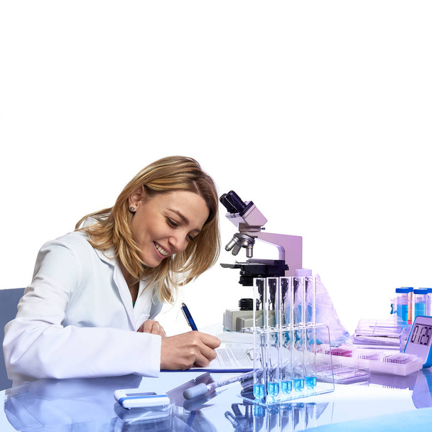 Young female scientist or tech writes report or lab journal in modern laboratory with microscope, glass tubes with samples and timer, This image is square, toned, isolated on white with copy-space. - Photo, image