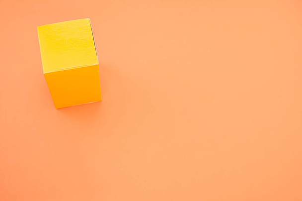 オレンジの背景に孤立した黄色い紙の立方体 - 写真・画像