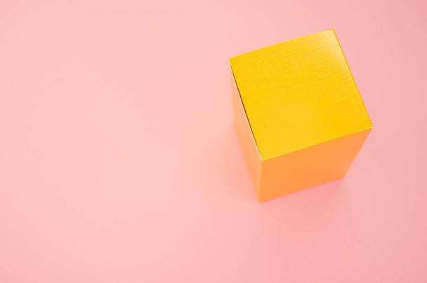A yellow paper cube isolated on a pink background - Foto, Imagen