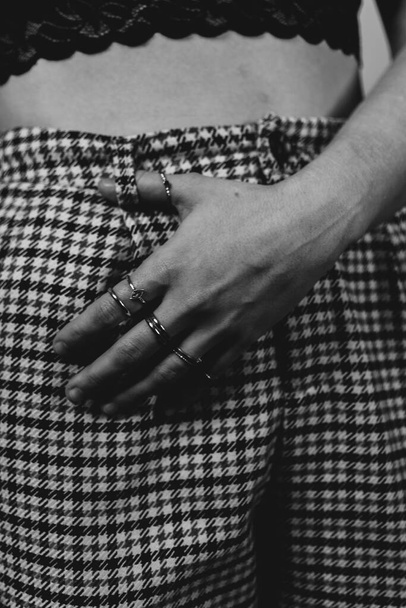 A grayscale shot of a female in checkered pants with many thin rings on the hand - Photo, Image