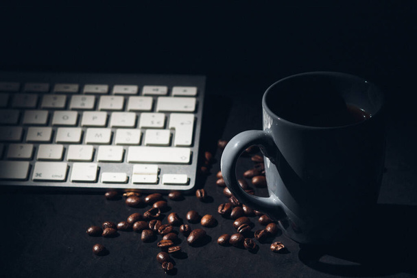A selective focus shot of a keyboard and a cup of hot coffee surrounded with beans - work from home concept - Zdjęcie, obraz