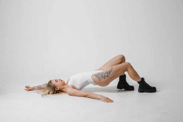 Fitted blonde in white bodysuit lies posing on a white background in black boots - Photo, image