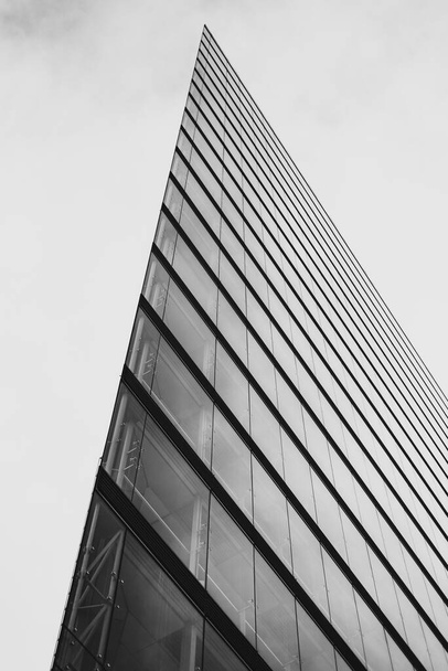 A vertical grayscale shot of a righ-rise modern glass-made offi building sharp corner - Foto, afbeelding