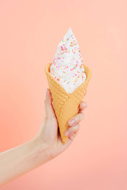 Жіноча рука тримає смачне м'яке морозиво зі зморшками у хрусткому вафельному конусі на рожевому тлі
 - Фото, зображення